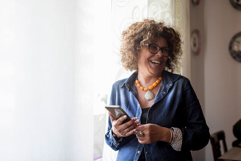 Smiling woman standing by window with mobile phone