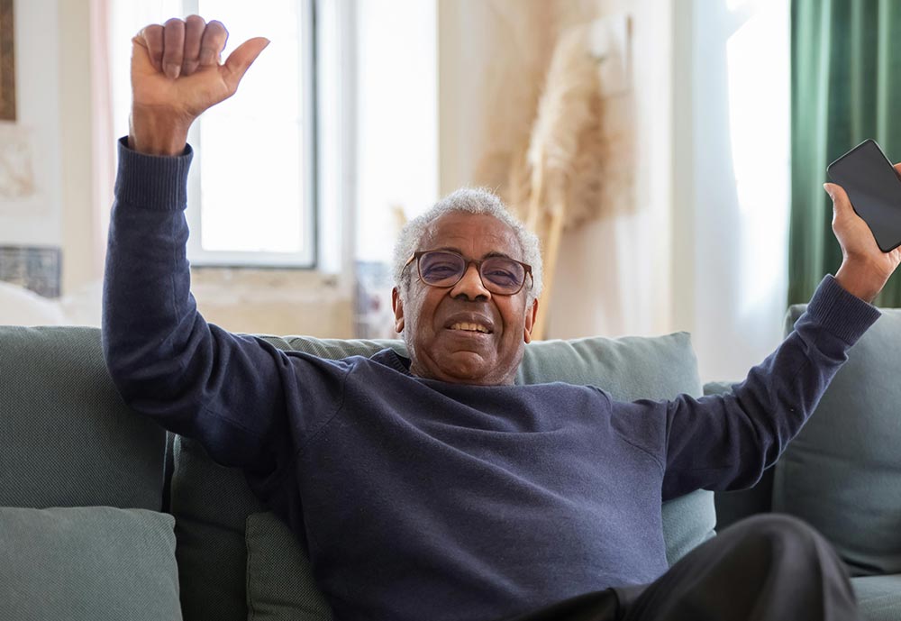 Satisfied older man celebrates a success with hands in the air hold a mobile phone